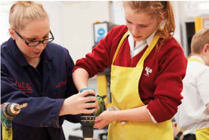 Prep School girl drilling hole into wood and teacher helping