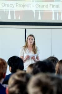 Hurst College Sixth Form student delivers a presentation during the Oracy Project Grand Final, speaking to an audience.